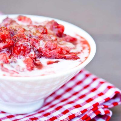 A bowl of this Strawberry Fool Recipe sits topped with some fresh, crushed strawberries.