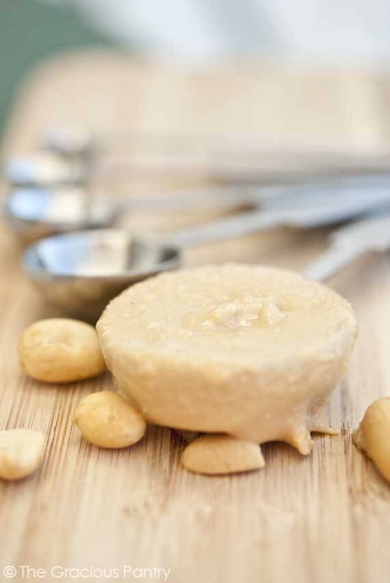 A tablespoon sits on a cutting board filled with peanut butter that is dripping over the edge of the spoon. Peanuts are also scattered about. It shows what is clean peanut butter.... just peanuts.