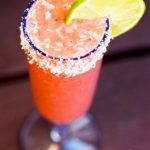 A delicious, strawberry daigquiri smoothie in a clear champagne glass, rimmed in coconut and garnished with a lime slice.