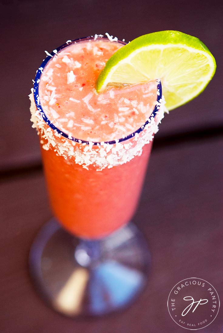 A delicious, strawberry daigquiri smoothie in a clear champagne glass, rimmed in coconut and garnished with a lime slice.