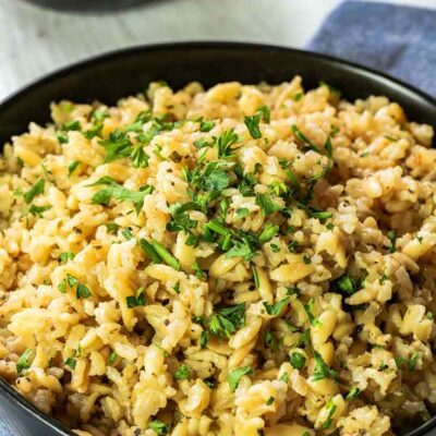 A bowl or delicious, brown rice pilaf sits in a black bowl, ready to serve and enjoy.