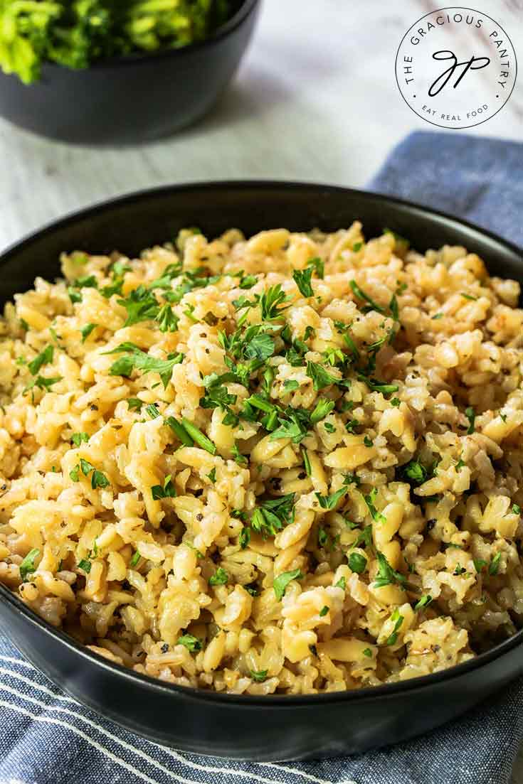 A bowl or delicious, brown rice pilaf sits in a black bowl, ready to serve and enjoy.