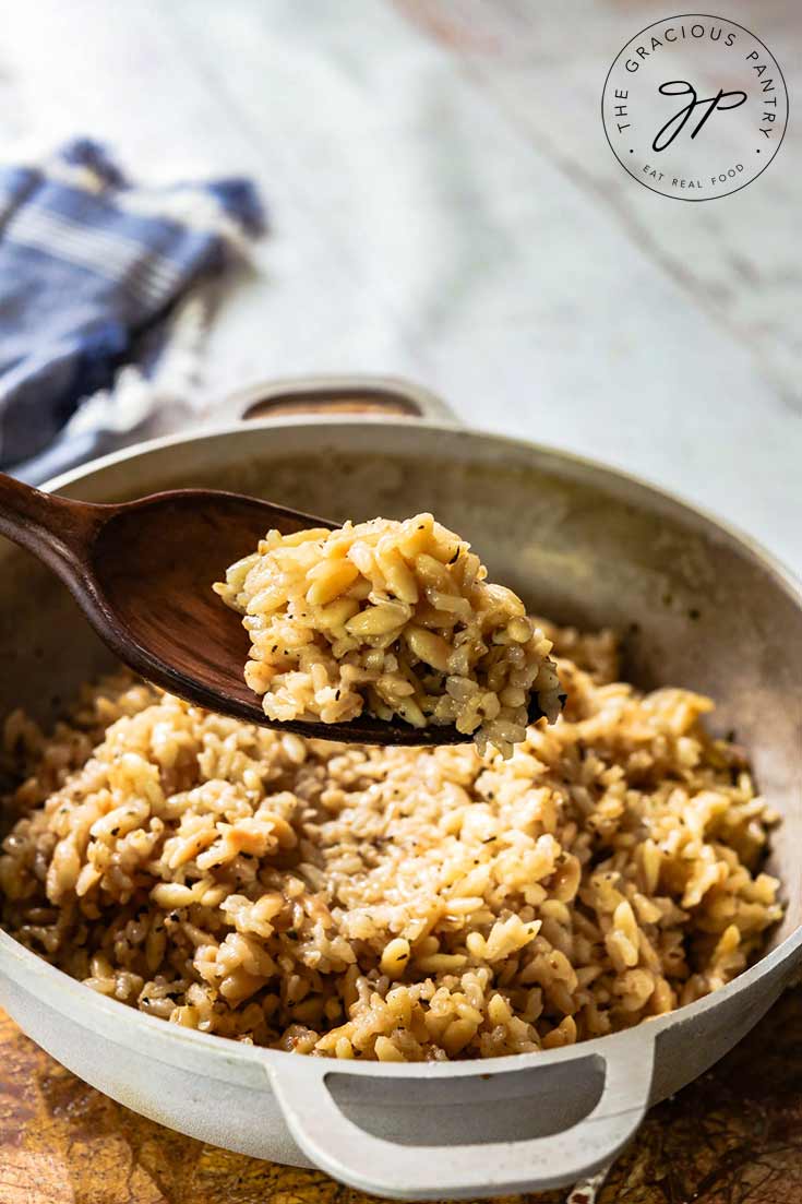 A serving dish filled with this Rice Pilaf Recipe is being served with a serving spoon at the dinner table.