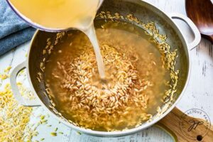 Adding the chicken broth to the roasted orzo.
