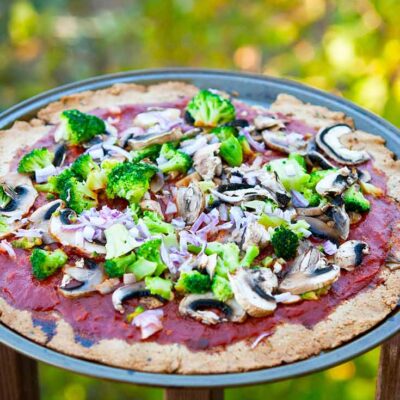 A full pizza sits on a pizza tray and was made with tha Thin Crust Pizza Dough. It's topped with red sauce, broccoli and onions.