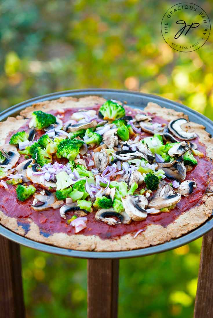 A full pizza sits on a pizza tray and was made with tha Thin Crust Pizza Dough. It's topped with red sauce, broccoli and onions.