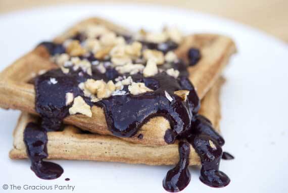 Clean Eating Blueberry Sauce poured over waffles with a few nuts sprinkled on top.