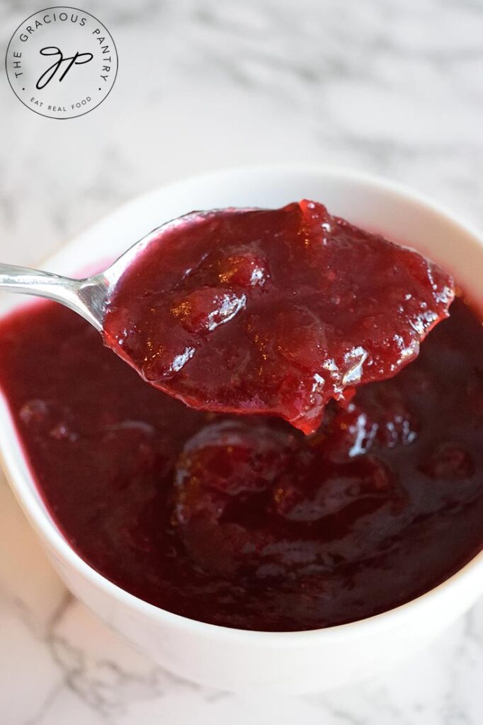 Thinner slow cooker cranberry sauce, scooped up on a spoon over the serving bowl.