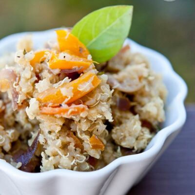 A white bowl sits filled with this Vegetable Quinoa Recipe and is garnished with a green leaf.