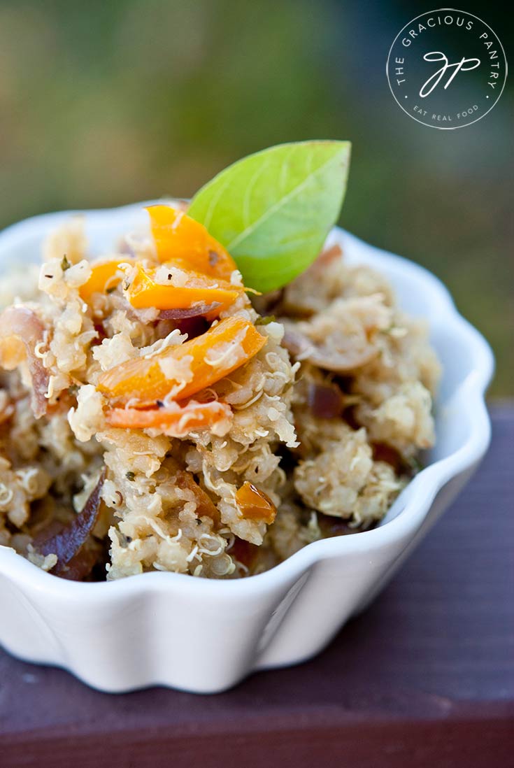 A white bowl sits filled with this Vegetable Quinoa Recipe and is garnished with a green leaf.