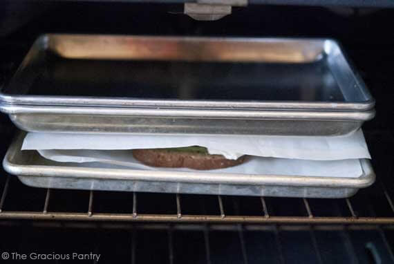 A grownup grilled cheese sandwich between baking pans and parchment in the oven.