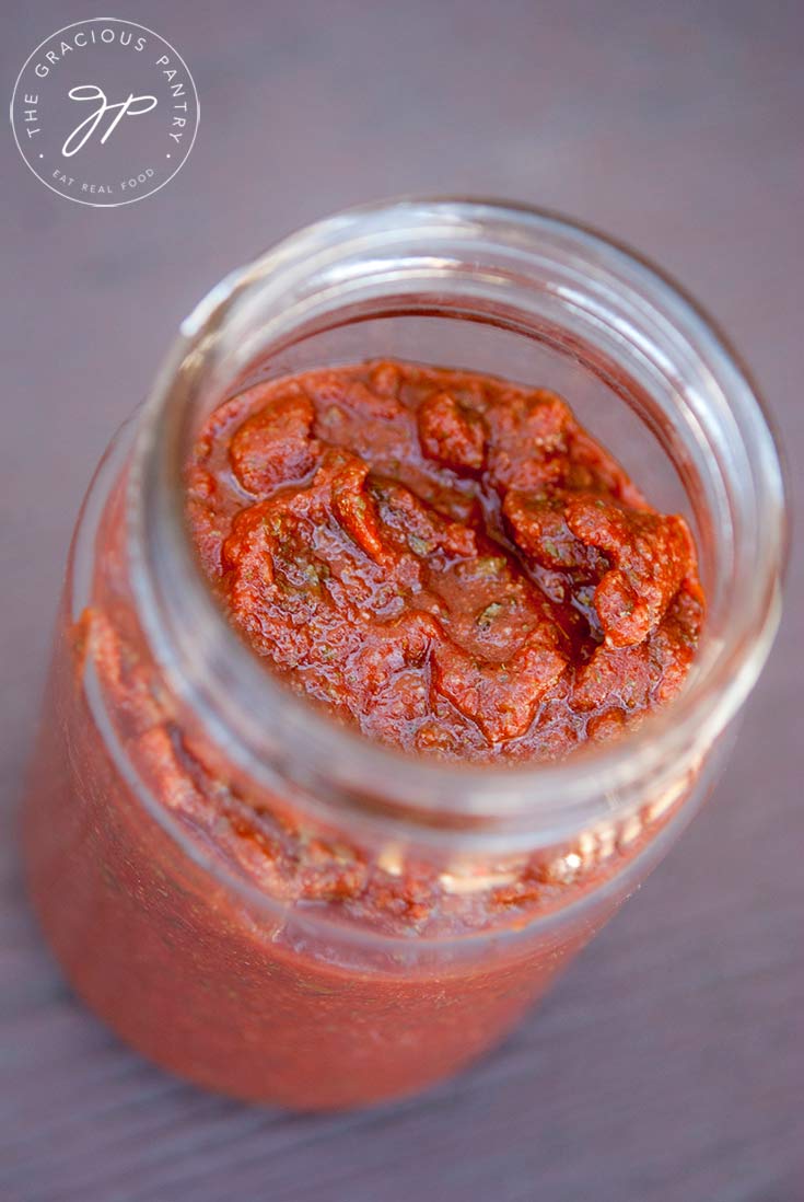 This Clean Eating Herbal Pizza Sauce Recipe sits in a n open jar. You can see down into the jar and the red sauce is thick and filled with herbs.
