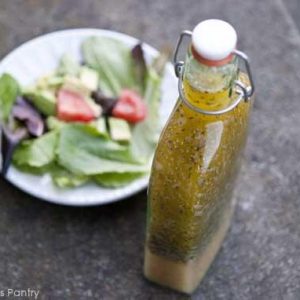 A bottle of homemade italian dressing sits next to a salad in a white bowl.