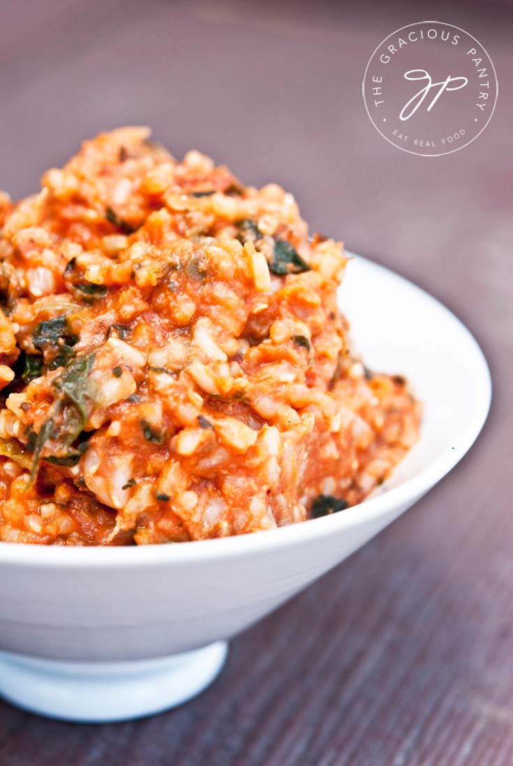 A small white bowl holds a heaping serving of this Clean Eating Spaghetti Rice With Spinach. The sauce is mixed in with the rice and you can see flecks of spinach everywhere throughout the rice.