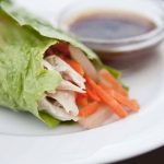 A single wrap from this Asian Lettuce Wraps recipe sits on a plate next to dipping sauce, ready to enjoy.