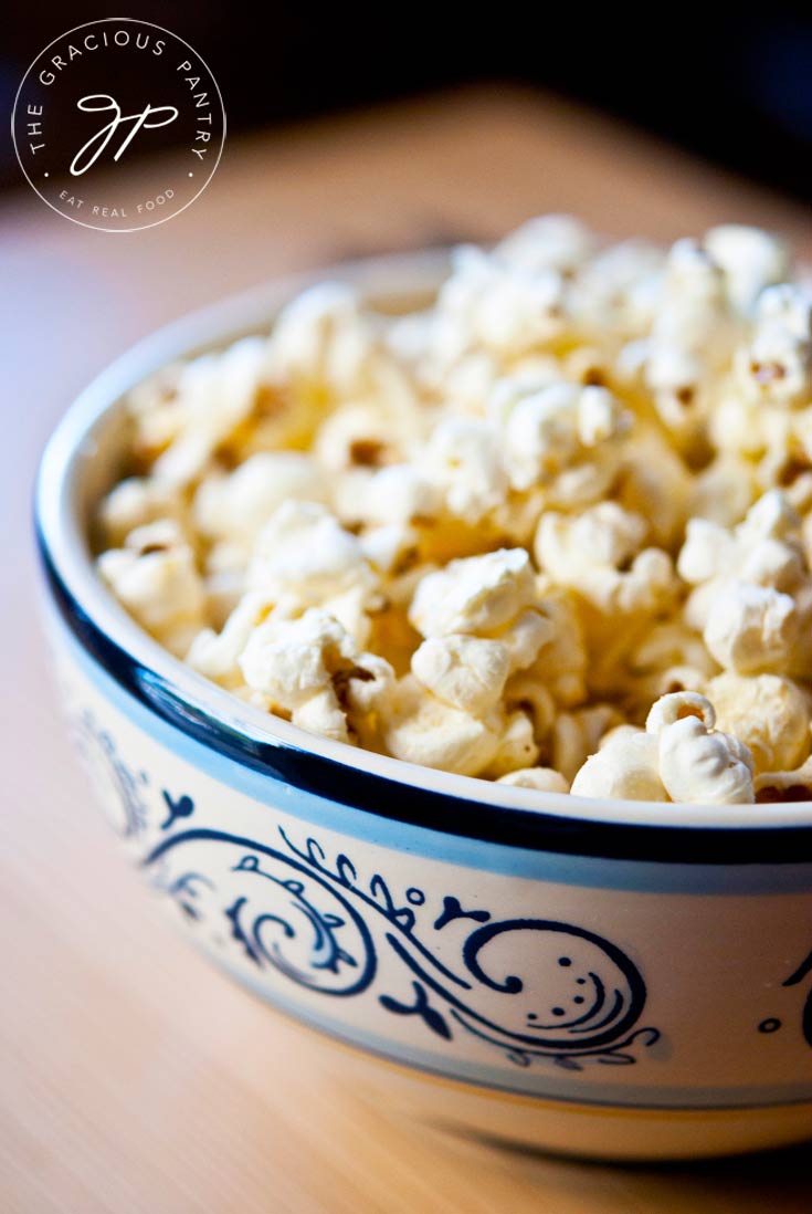 A blue and white bowl of Clean Eating Garlic Parmesan Popcorn sits on a wooden table with a black background.