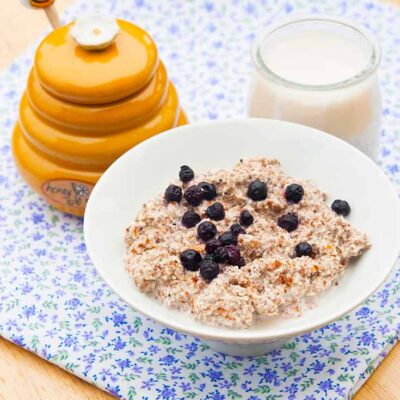 A bowl of this Almond Porridge sits next to a yellow honey pot and a small container of milk.