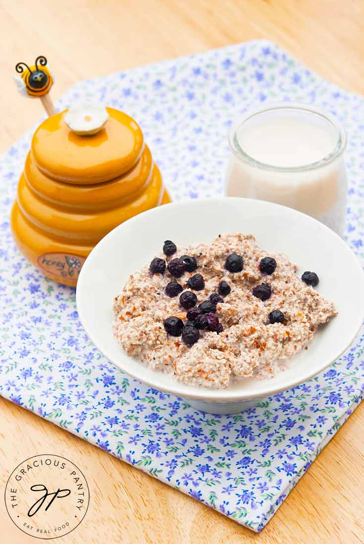 A bowl of this Almond Porridge sits next to a yellow honey pot and a small container of milk.