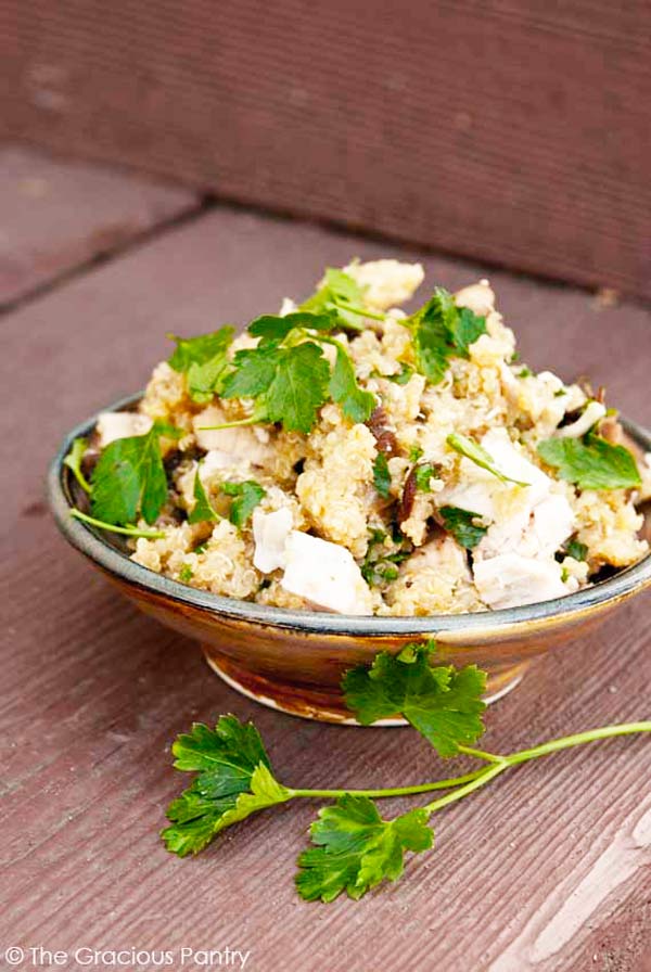 An earthen bowl sits on a wooden surface, filled with Clean Eating Mushroom Quinoa. Fresh parsley has been sprinkled over the quinoa and a sprig of it also sits to the side of the bowl.