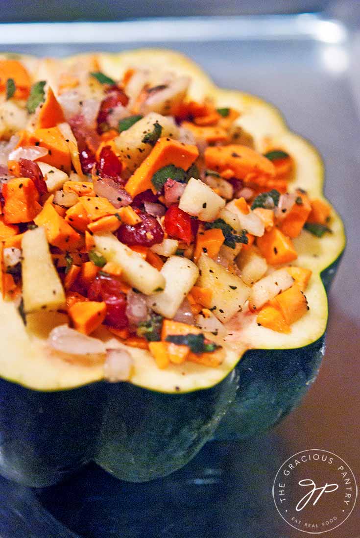 A stuffed acorn squash sits on a baking pan, ready to put into the oven to bake.