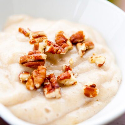 A bowl of easy banana pudding sits on a table, topped with chopped nuts.