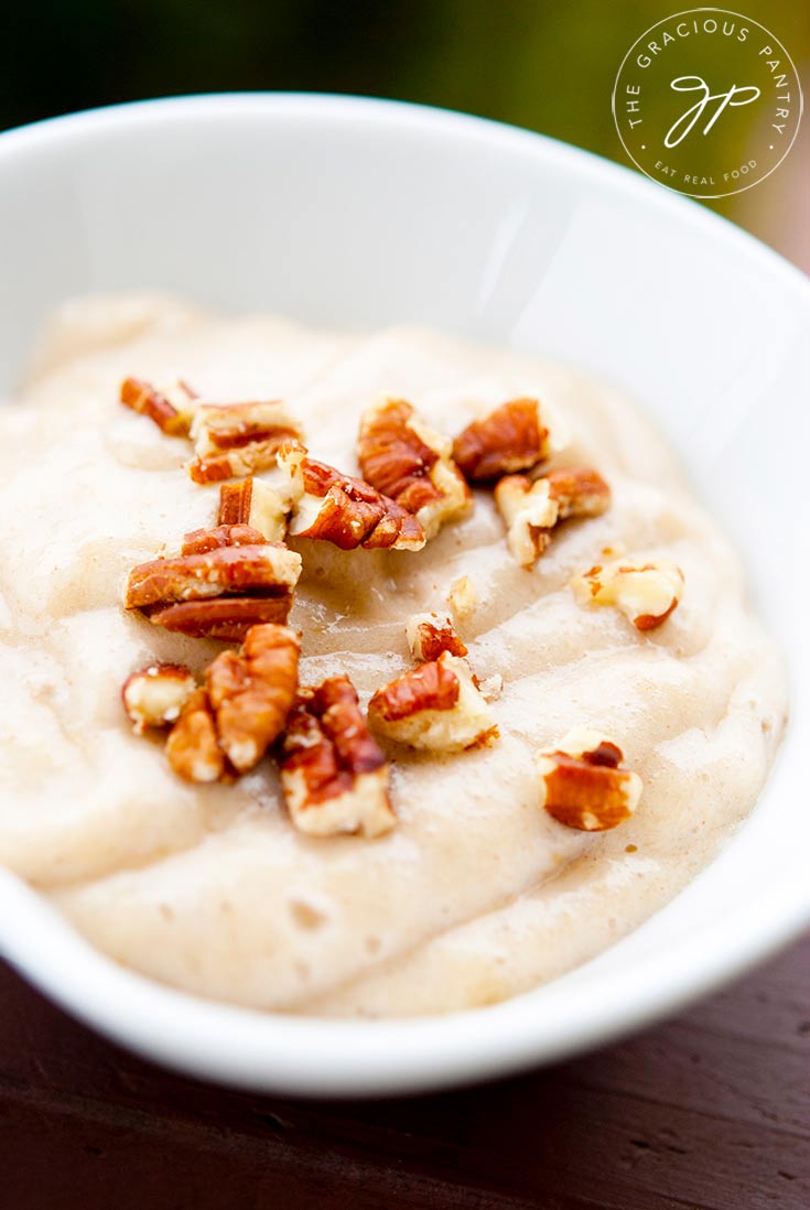 A bowl of easy banana pudding sits on a table, topped with chopped nuts.