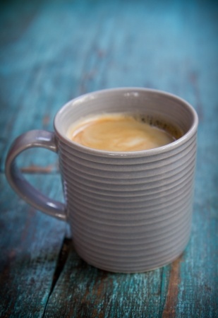 A mug of coffee sitting on a rustic blue surface.