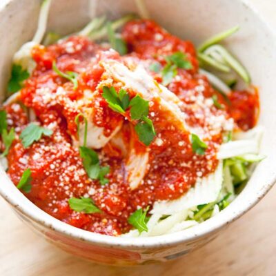 A bowl sits filled with this Baked Chicken Marinara. Zucchini noodles lay under the chicken and marinara giving it a lovely pop of green.