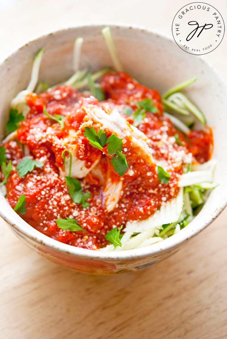 A bowl sits filled with this Baked Chicken Marinara. Zucchini noodles lay under the chicken and marinara giving it a lovely pop of green.