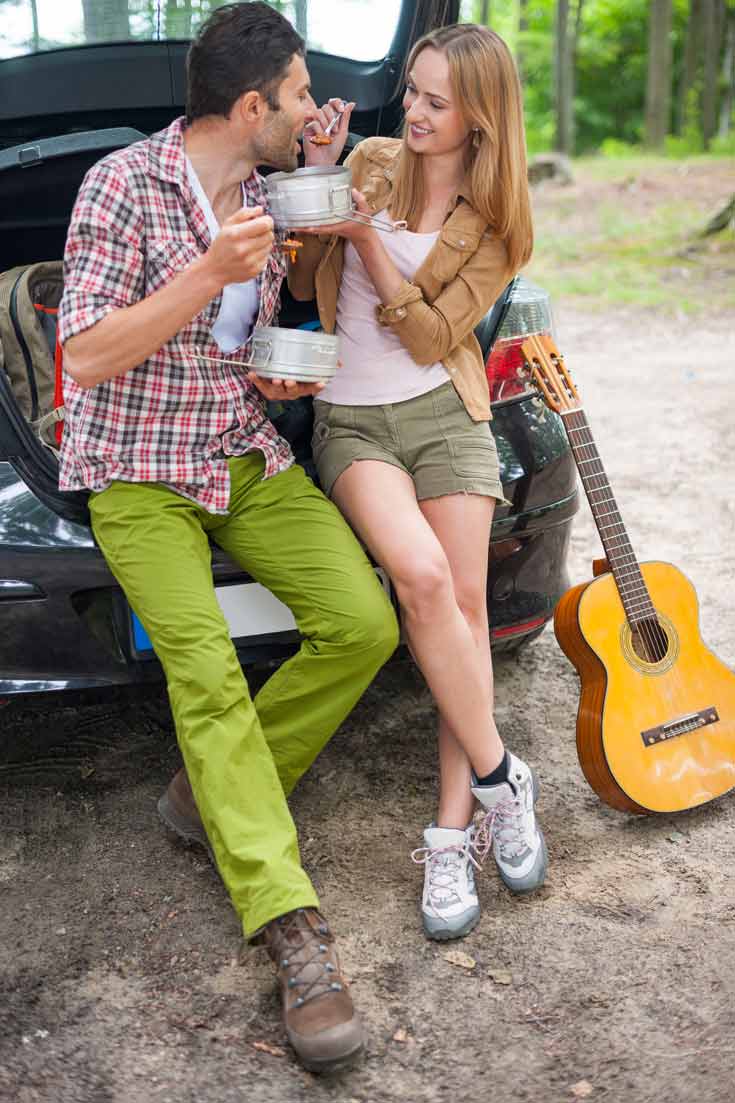 A couple enjoying healthy tailgate style lunch in the woods. The hatch of their car is open and they are enjoying their meal from tin containers. You can't see what they are eating specifically, but I'm going to guess it's probably one of these 40 clean eating road trip snacks!