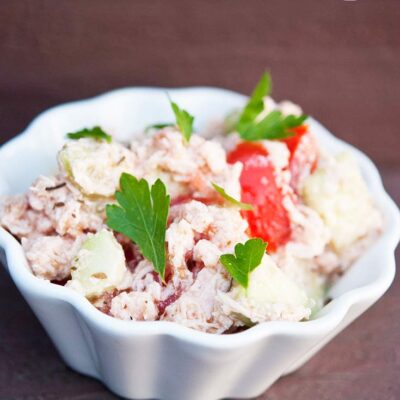 A white bowl filled with this Chicken And Cucumber Salad sits garnished with parsley and ready to eat.