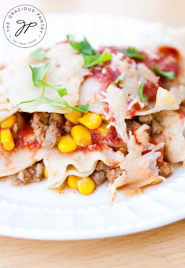 Clean Eating Mexican Lasagna shown on a white plate, up close, so you can see the layers of noodles, ground turkey, corn and sauce.