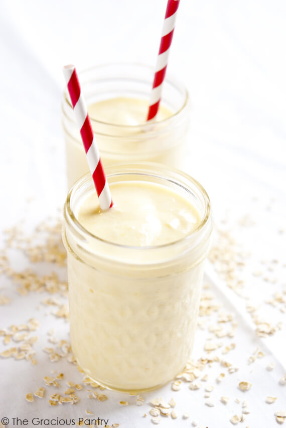 Two pint size canning jars filled with Mango Oatmeal Smoothie. Both jars have red and white striped straws in them.