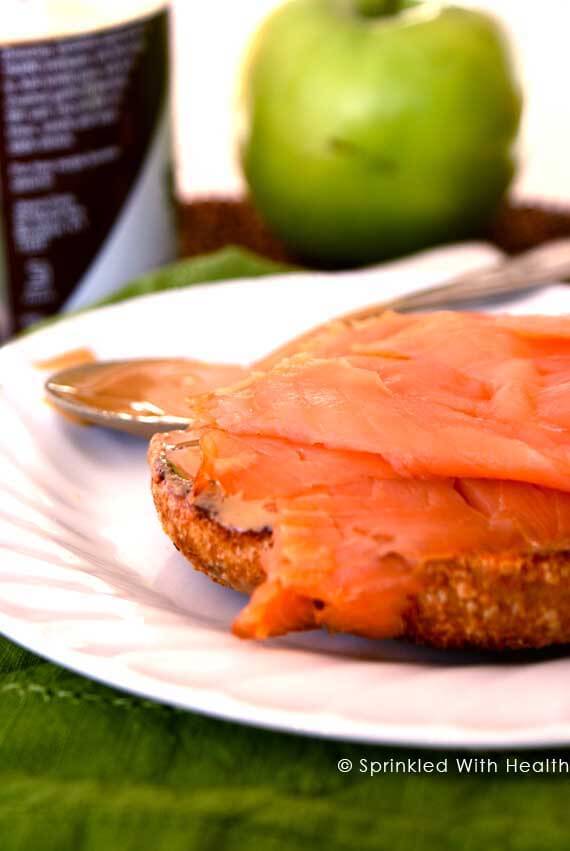 A cut bagel with smoked salmon on top, sits on a white plate.