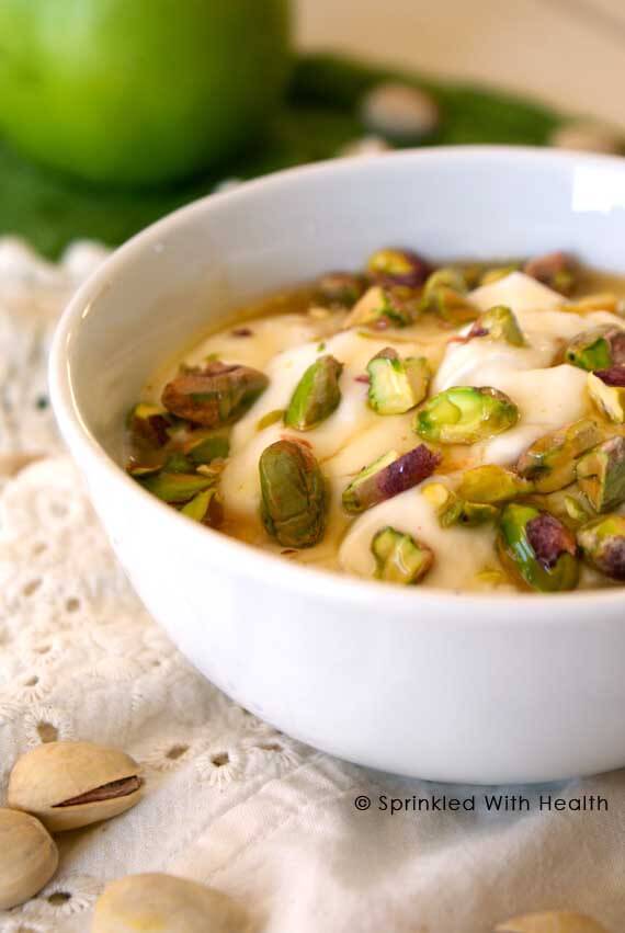 A white bowl of greek yogurt with pistachios sprinkled over the top.