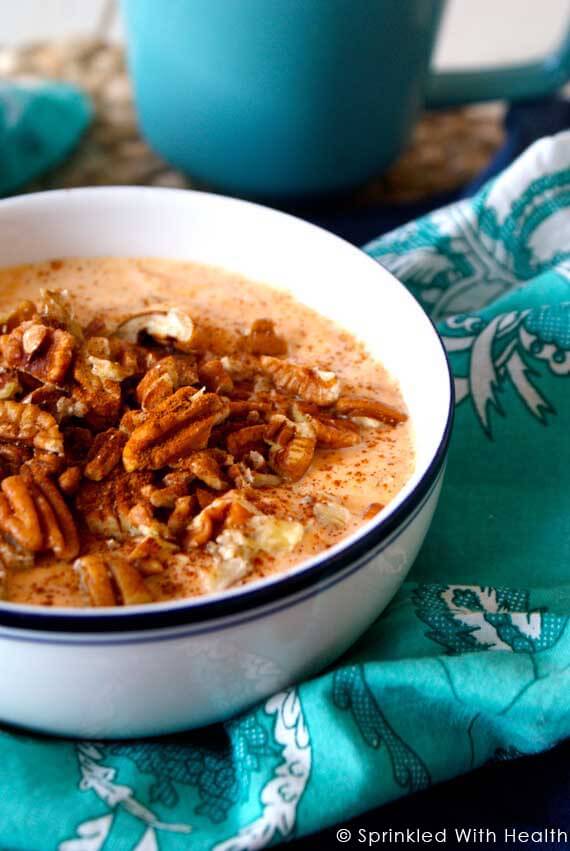 A white bowl sits on a towel, and is filled with pumpkin pie greek yogurt and topped with pecans.