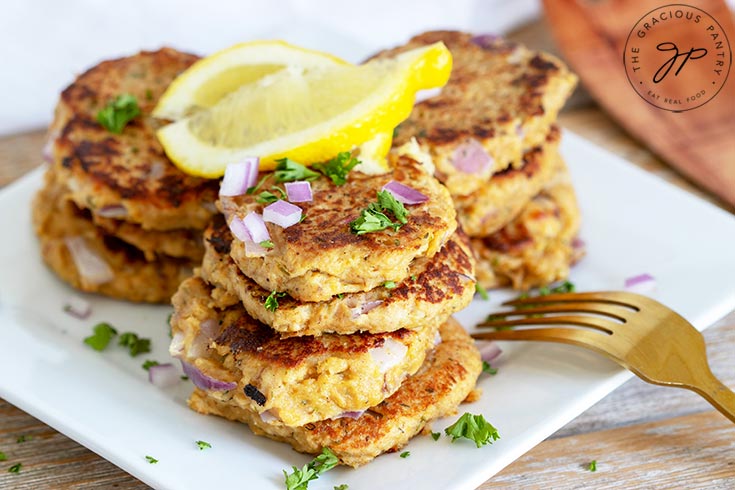 Freshly cooked, clean eating tuna patties sit on a plate with a lemon wedge, ready to eat.