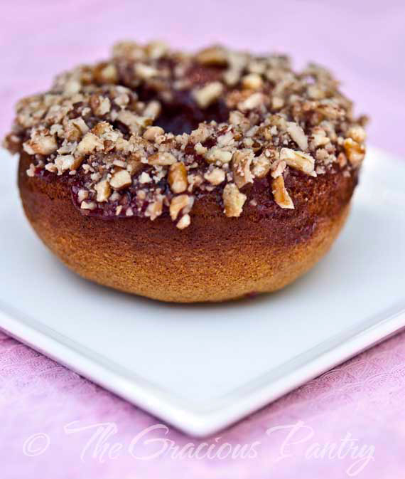 A single doughnut from this Clean Eating Doughnuts Recipe sits on a white, square plate. It's shown from the side. You can see the brown doughnut, the layer of fruit topping and the ground nuts sprinkled over the top.