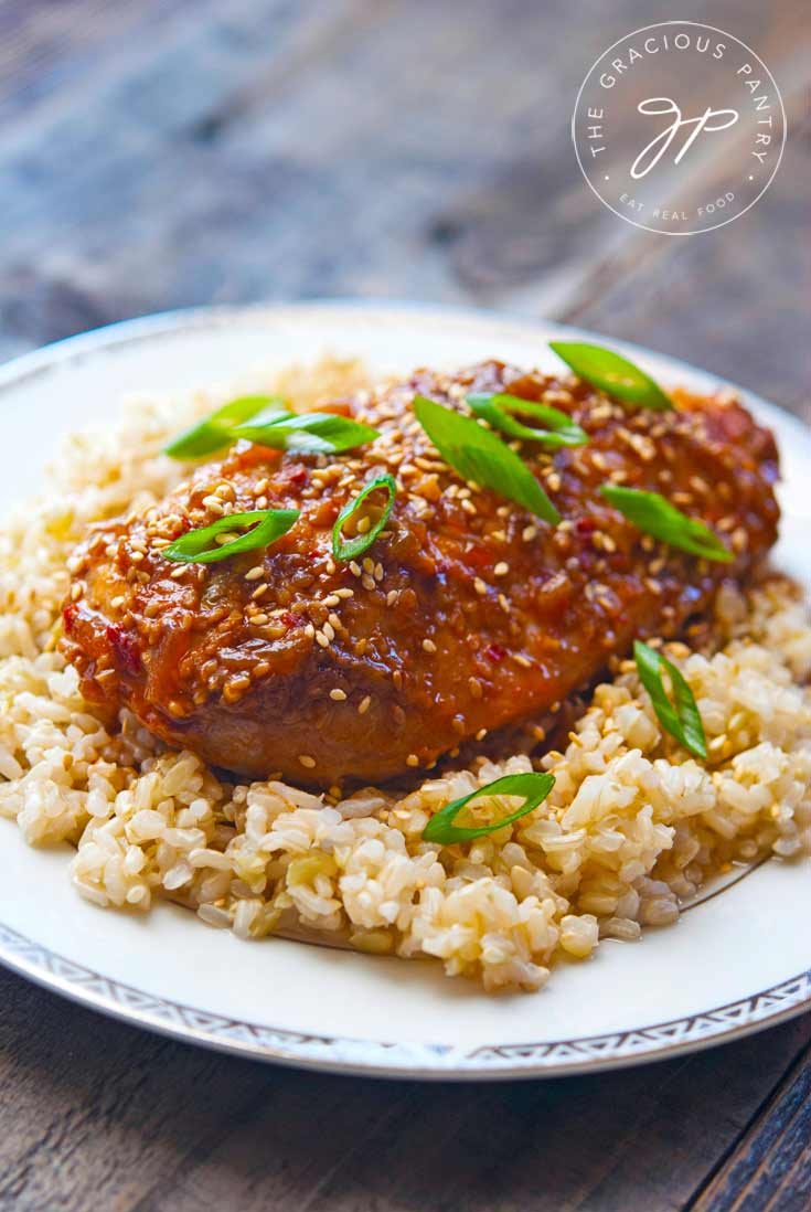 Clean Eating Slow Cooker Honey Sesame Chicken Recipe showing the glazed chicken sitting on a bed of brown rice with sliced green onions lightly sprinkled on top.