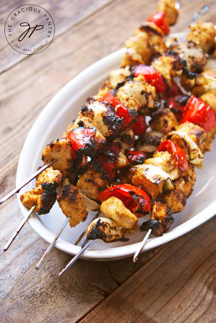 A pile of Mexican chicken skewers sits on a white platter, ready to eat.