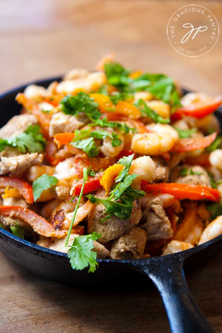 A black, cast iron skillet sits filled with this Clean Eating Barbecued Southwestern Chicken And Shrimp Skillet recipe. It's topped with fresh cilantro.