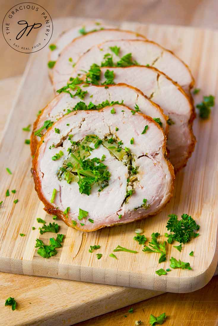 A sliced turkey roulade sits on a cutting board with the slices nicely arranges one on top of the other. They are sprinkled with fresh herbs.