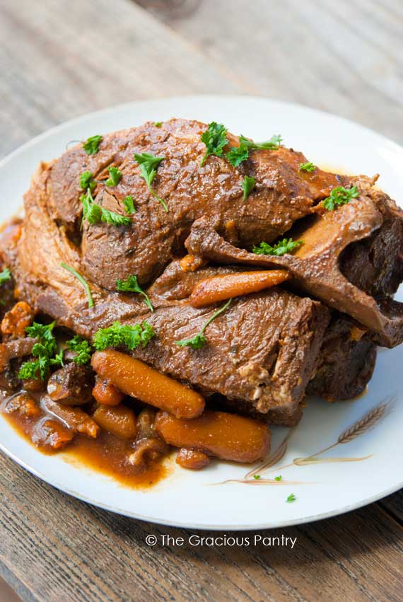 10 Hour Slow Cooker Clean Eating Pork Roast on a platter with some carrots and gravy around the roast with some chopped, green herbs sprinkled over the top for garnish.