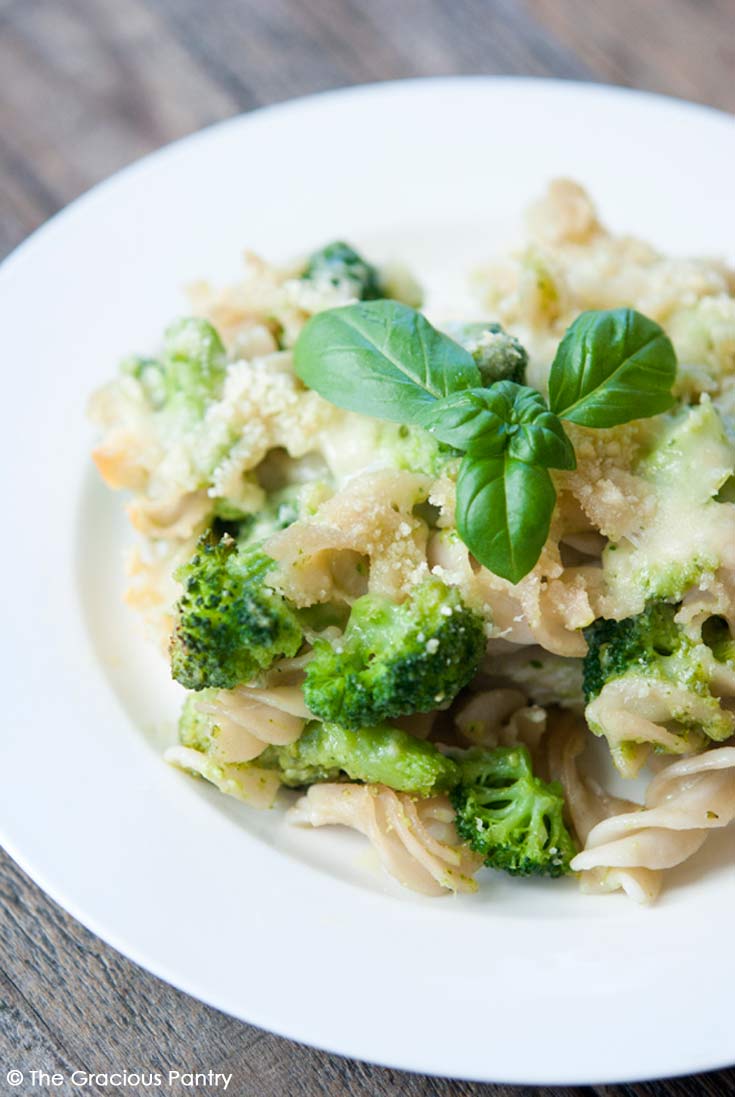 Clean Eating Pesto Broccoli Casserole served on a round, white plate. You can see the pasta, broccoli florets and a sprig of fresh basil sitting on top.