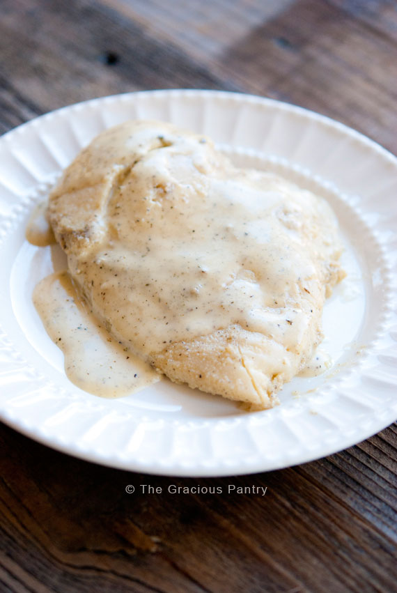Two breasts of chicken on a white plate with Italian dressing ladled over the top show this Clean Eating Slow Cooker Italian Chicken recipe.