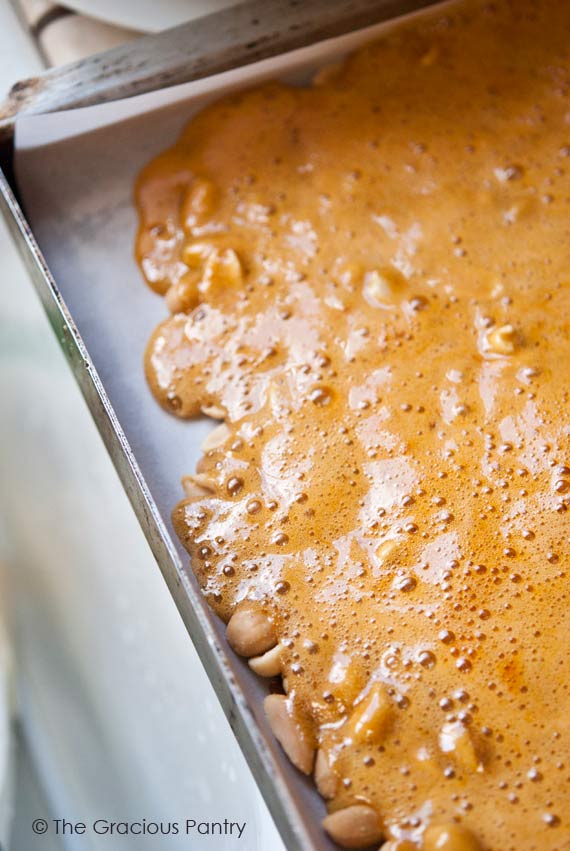 Peanut brittle mixture cooling on a parchment-lined baking sheet.