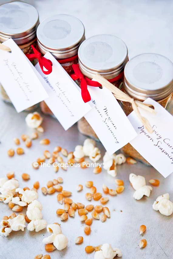 Four bottles of Clean Eating Popcorn Seasoning Recipes standing in a row with red bows tied around them showing that these make great personalized gifts for the holidays.