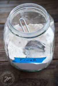 A large jar holding flour with a measuring cup sitting inside.