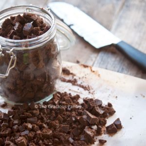 Homemade Mint Chocolate Chips in an open glass jar that sits on a cutting board with more chocolate chips.