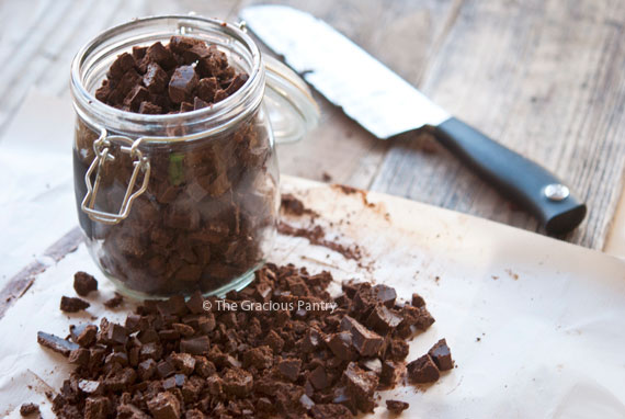 Homemade Mint Chocolate Chips in an open glass jar that sits on a cutting board with more chocolate chips.
